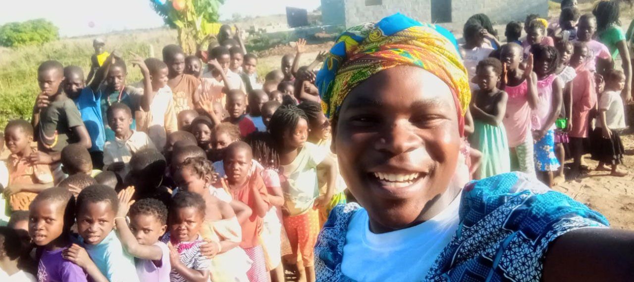 Smiling person in colorful headscarf taking a selfie with a large group outdoors