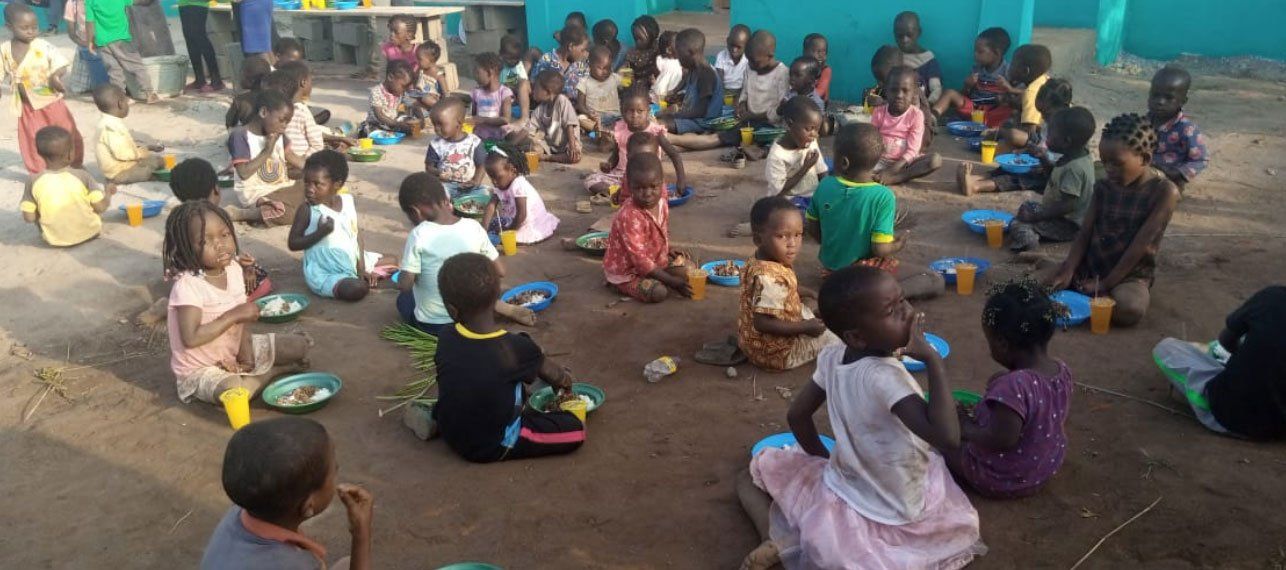 People seated in a circle outdoors, eating and talking during a community gathering.