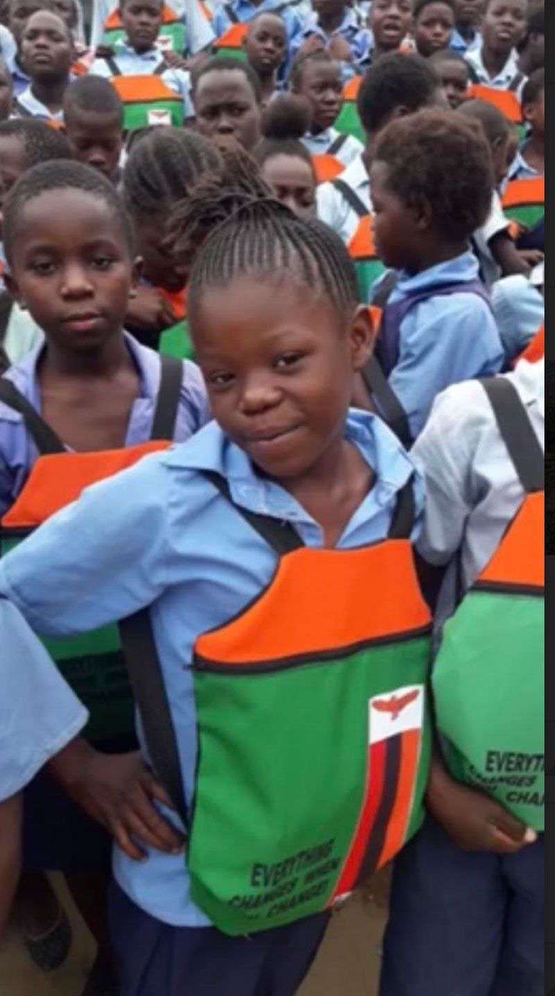 Children in school uniforms standing together, with one child in front wearing a green and orange bib.