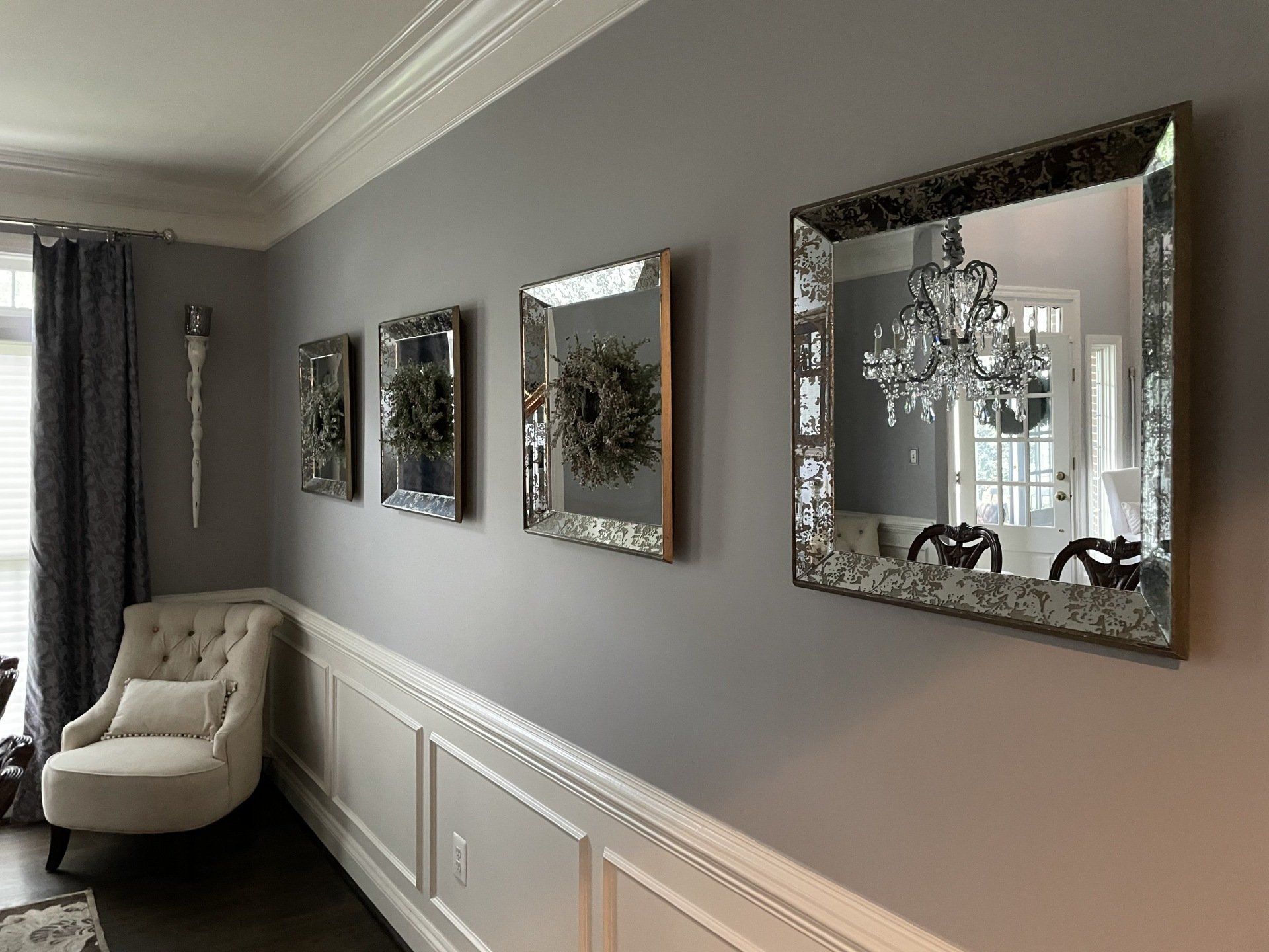 Gray dining room wall with three ornate mirrors and a white chair by a window