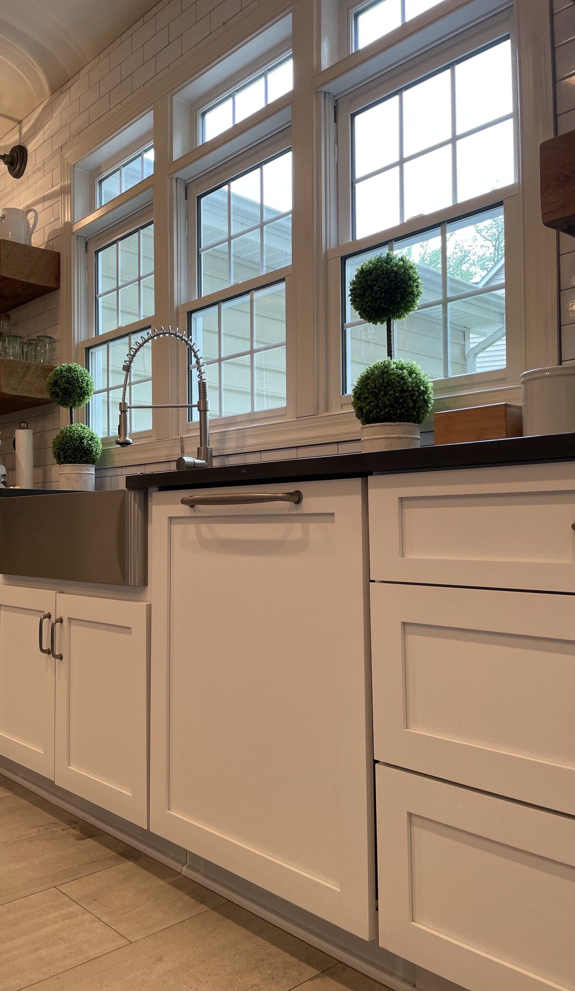White kitchen cabinets under bright windows with potted topiary plants on the counter.