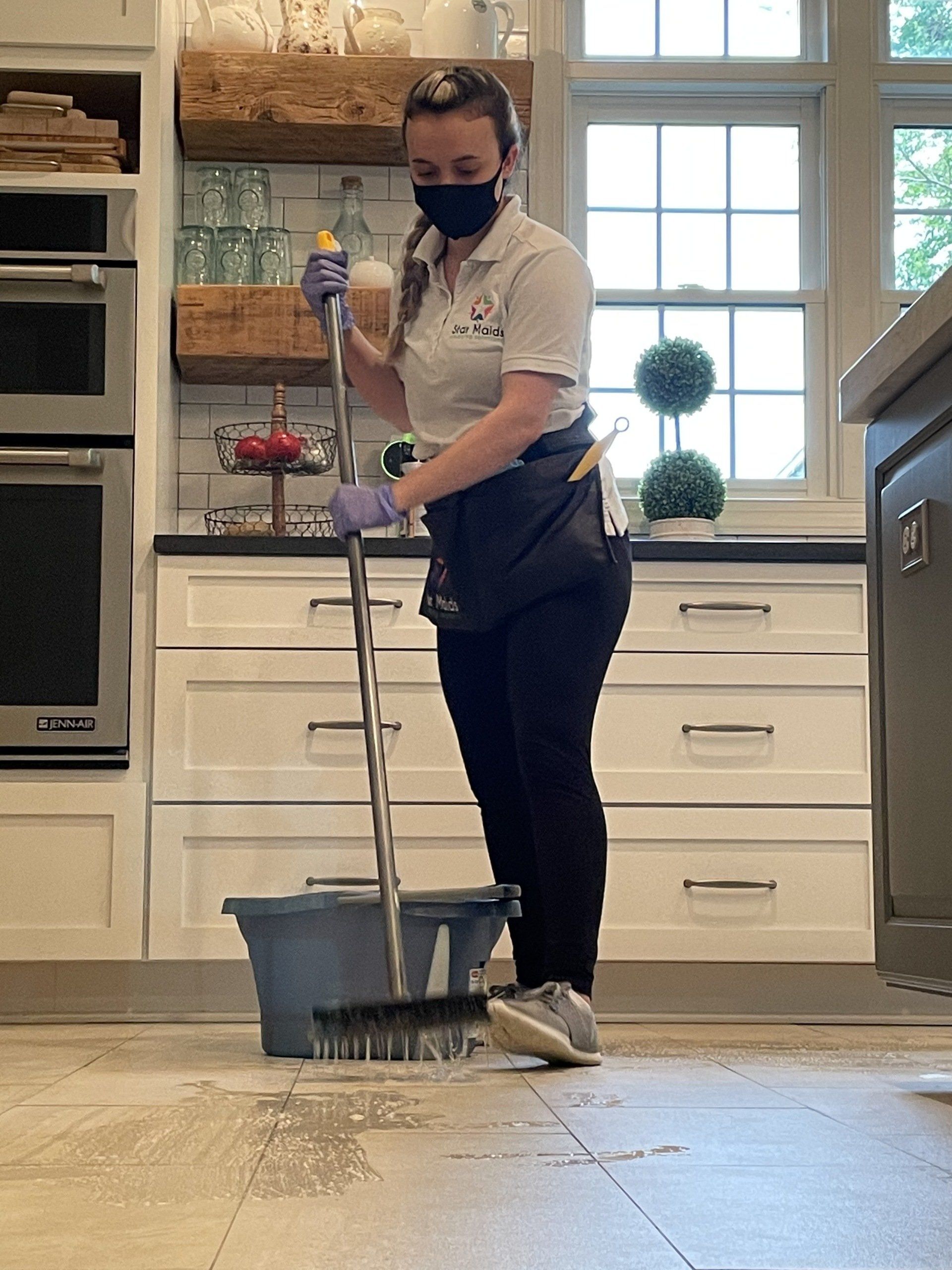 Person mopping a kitchen floor, wearing a mask and gloves.