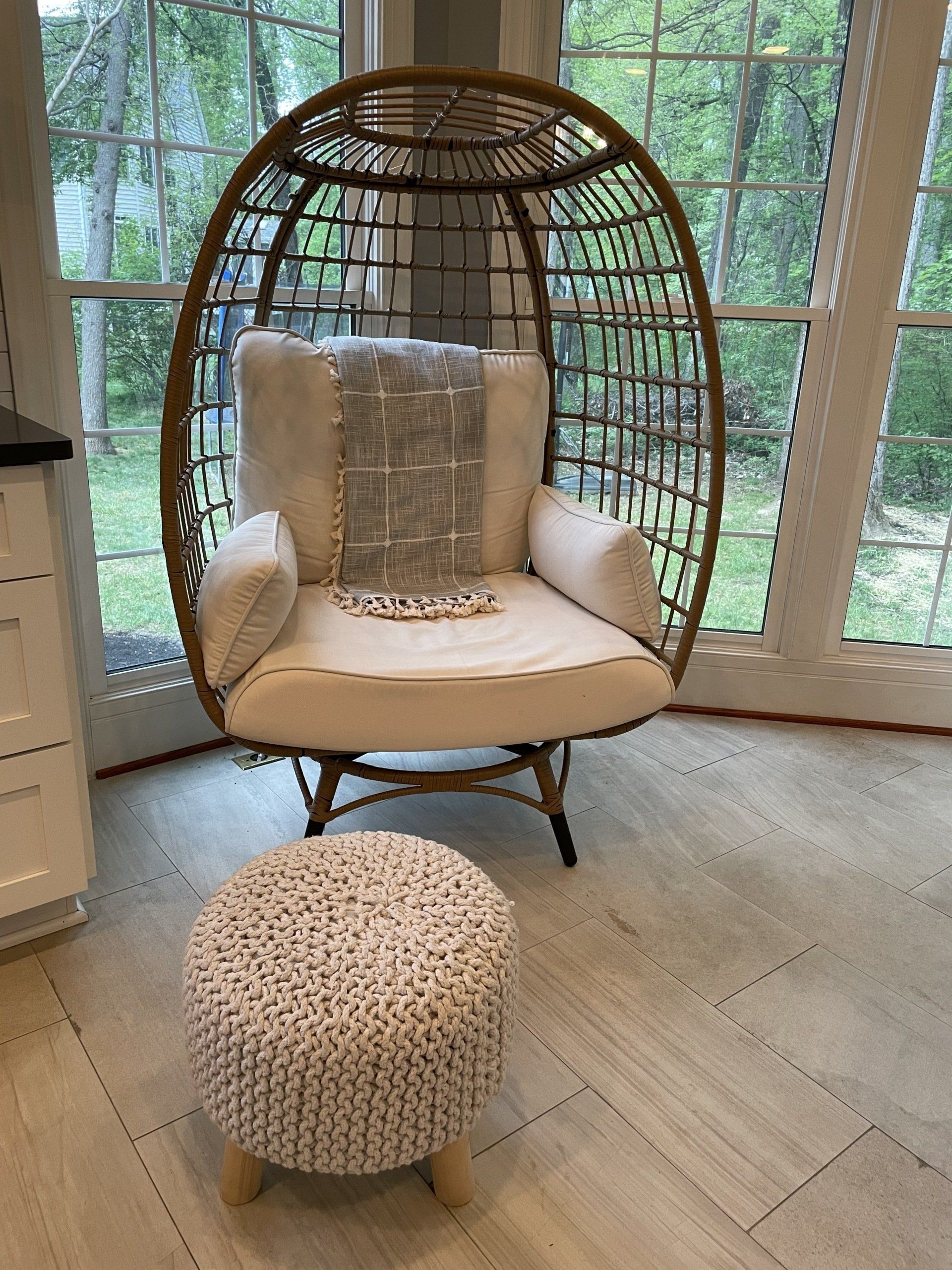 Wicker egg chair with cream cushion and ottoman by bright windows in a sunroom