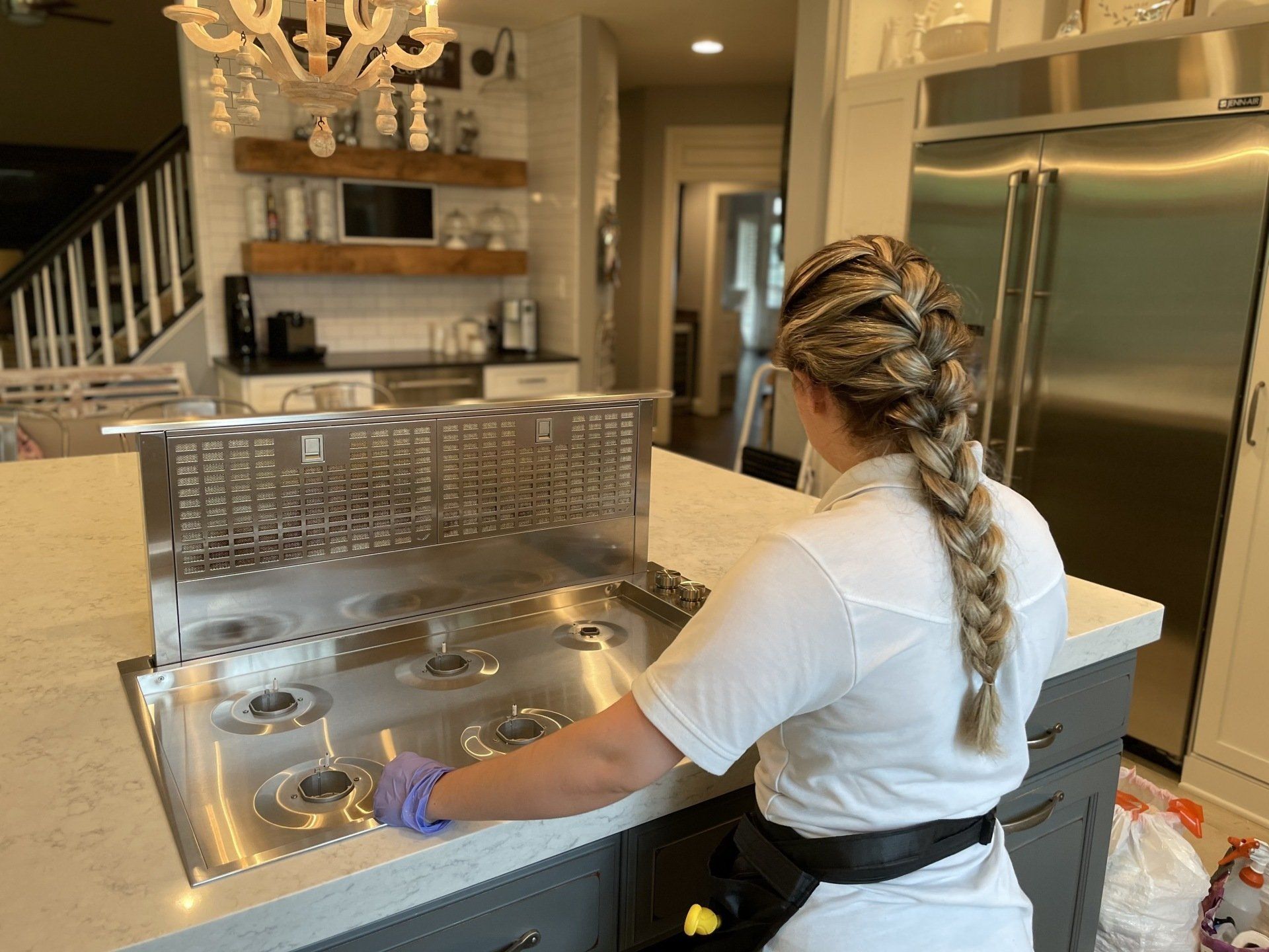 Person standing at a kitchen island preparing food, with stainless steel appliances and a chandelier in the background.