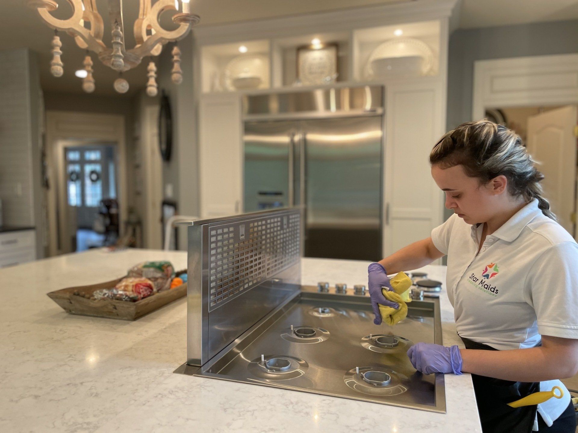 Person in purple gloves cleaning a stove in a modern kitchen