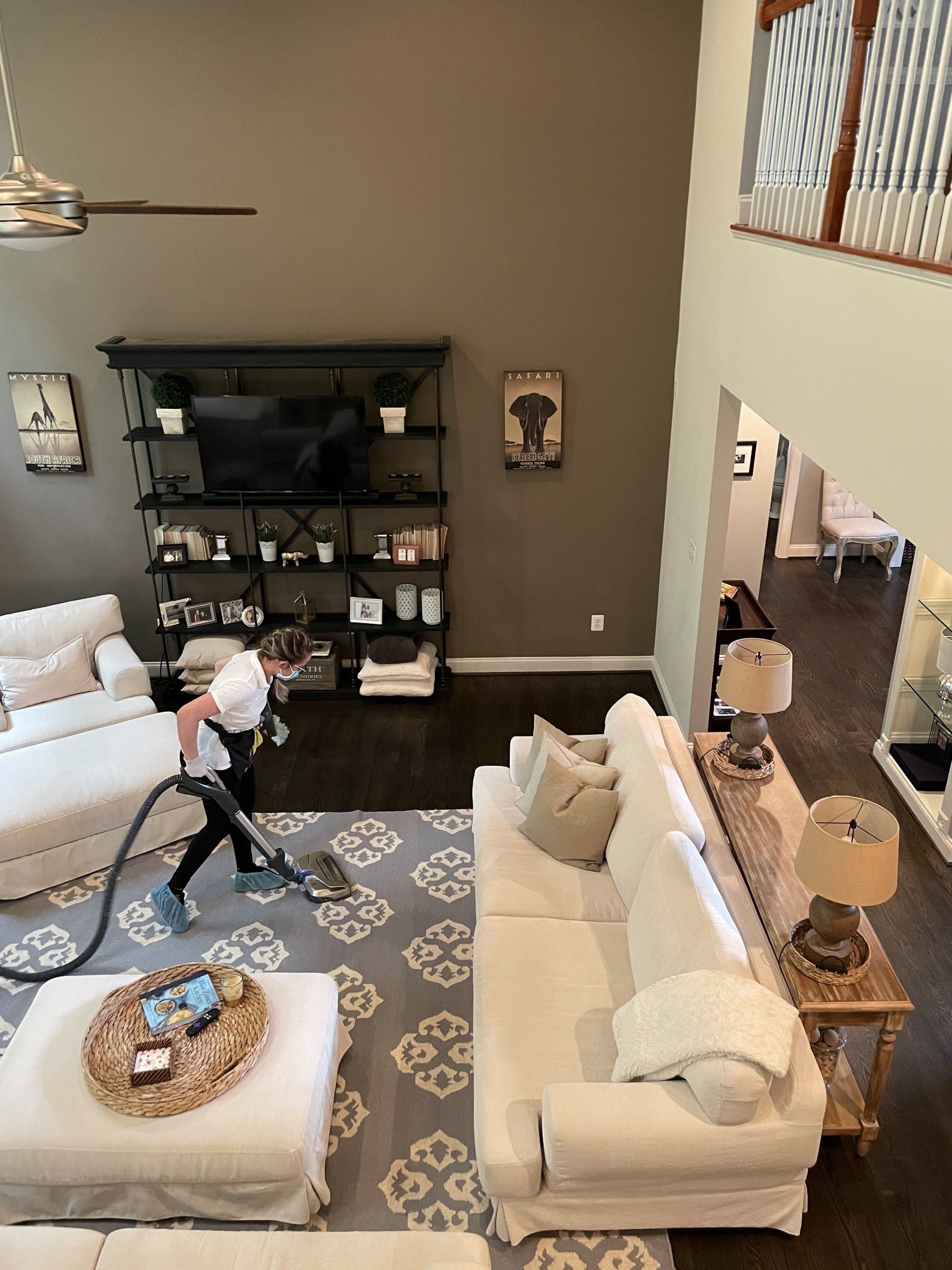 Living room with two sofas, patterned rug, and a person vacuuming near the TV console