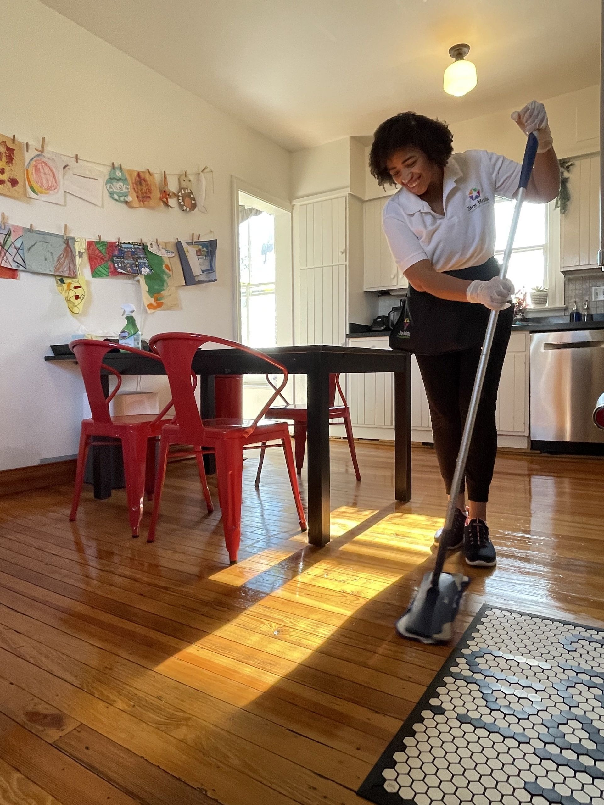 Person mopping a sunlit kitchen floor beside a table and red chairs