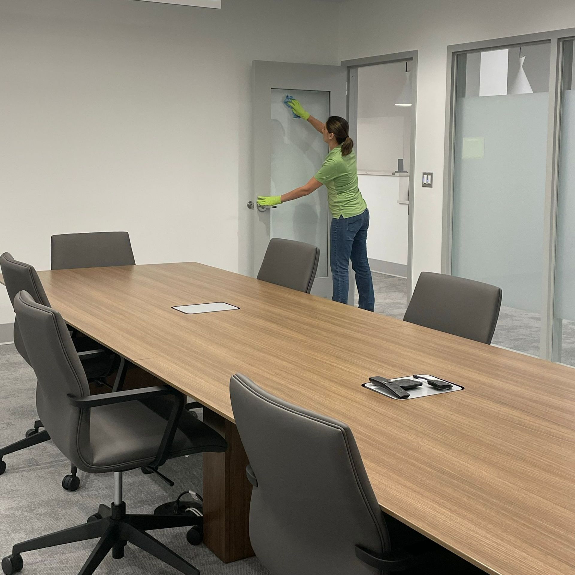 Person cleaning a conference room door beside a long wooden table and office chairs