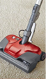 Red and gray upright vacuum cleaner on beige carpet