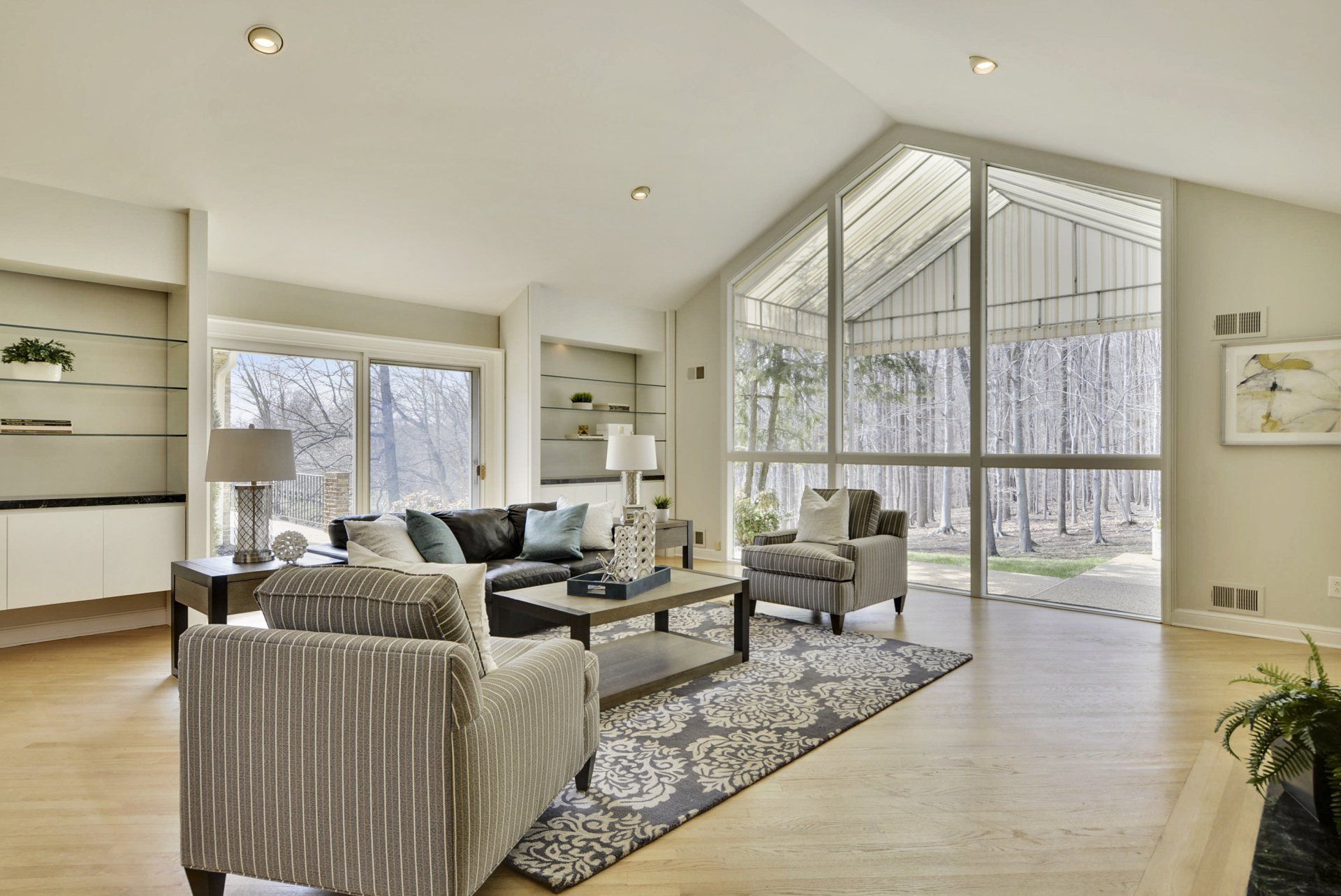 Bright living room with large windows, striped armchairs, gray sofa, and patterned rug