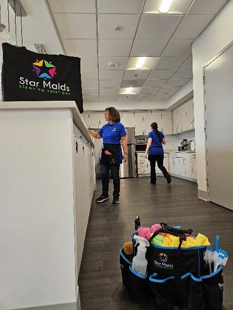 Two workers in a kitchen hallway carrying cleaning supplies, with a mop bucket in the foreground.