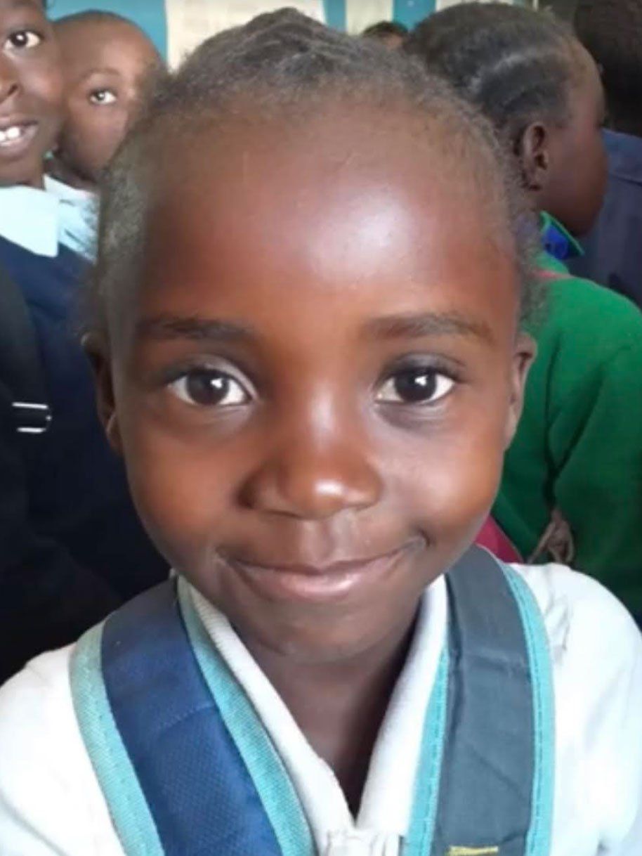 Smiling child in a blue school uniform standing in a classroom