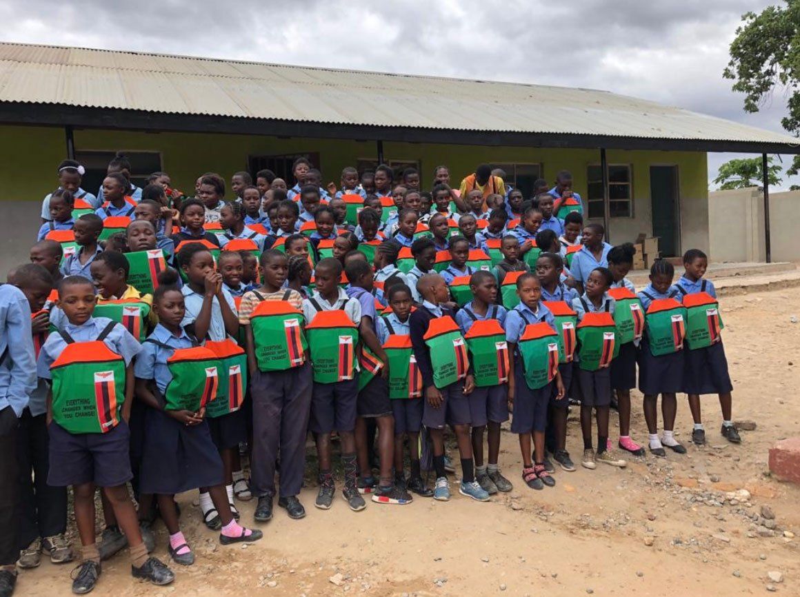Large group gathered outside a building, many holding green and orange folders or books