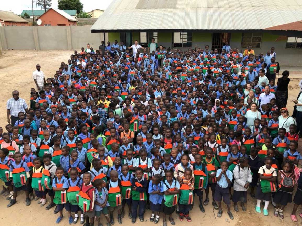 Large group of students in blue and green uniforms gathered outdoors in a school courtyard