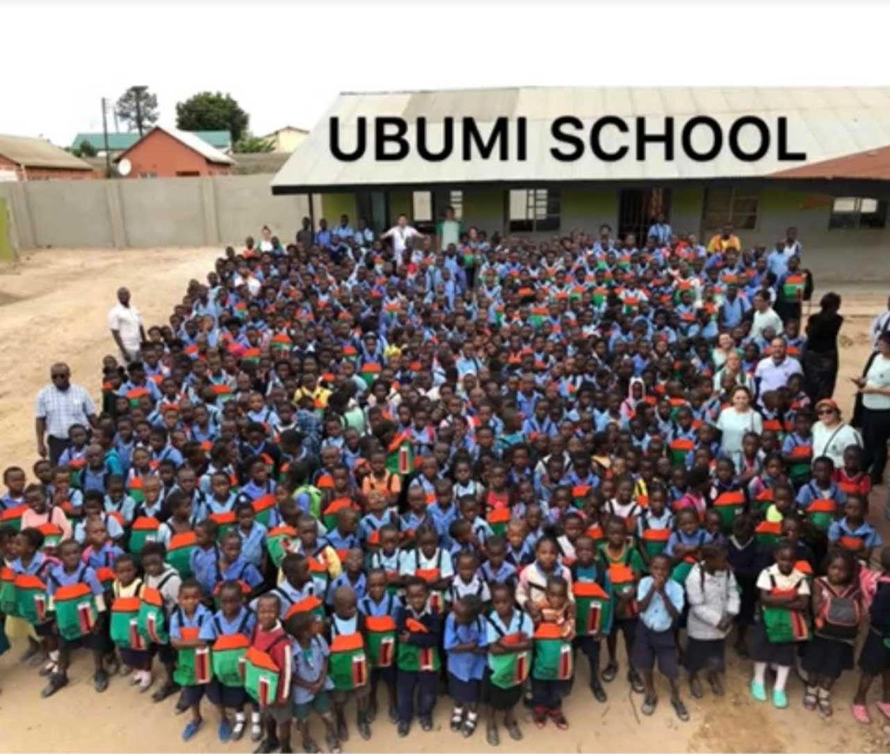 Large group of students posing outside Ubumi School building, wearing colorful uniforms.