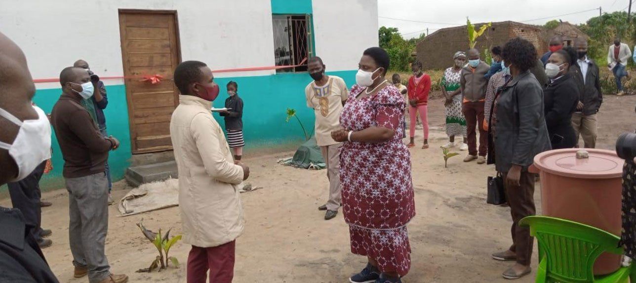 People standing apart outdoors near a turquoise building, some wearing masks and talking.