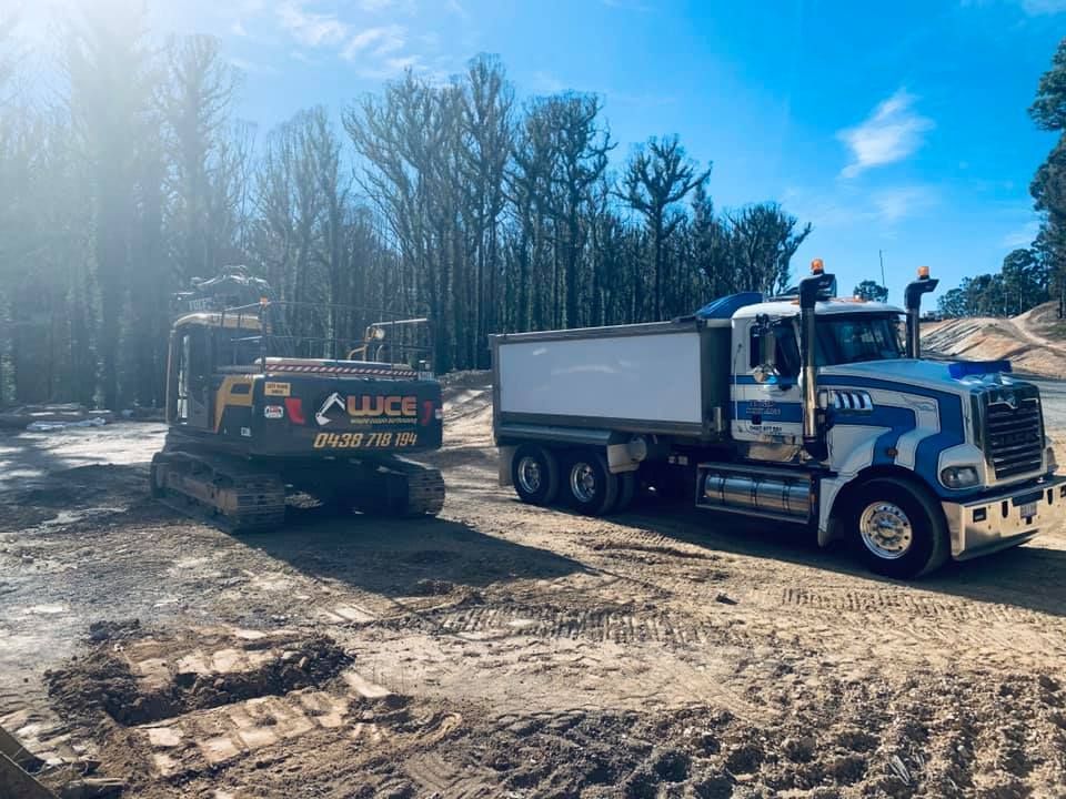 A dump truck is parked next to a bulldozer on a dirt road.