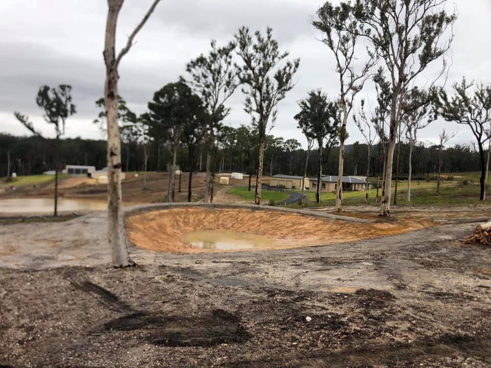 A small pond in the middle of a dirt field with trees in the background