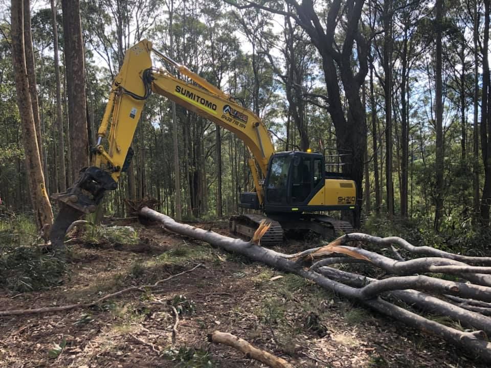 A yellow excavator is digging a hole in the middle of a forest.