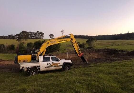 A yellow excavator is digging a hole in a field next to a truck.