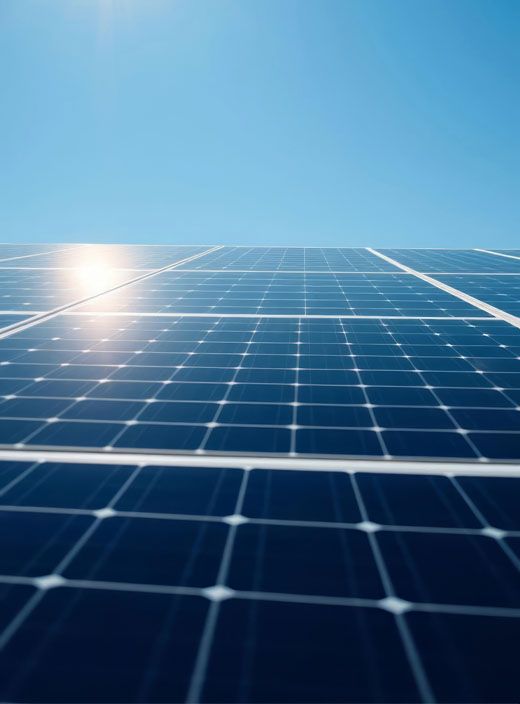 A row of solar panels against a blue sky with the sun shining through them