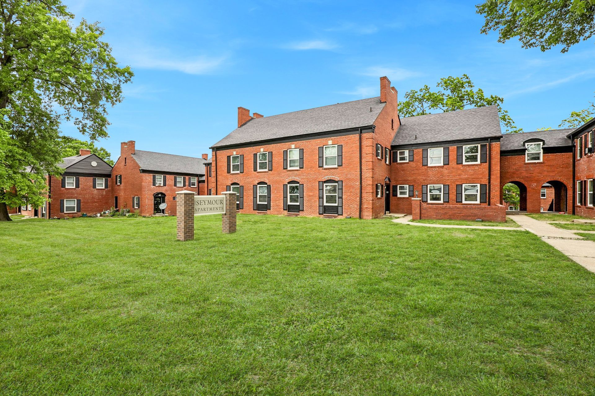 Brick apartment buildings with symmetrical windows, The Seymour sign, set on green lawns under a blue sky.