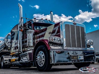 Chrome-covered semi-truck with maroon and white accents parked against a blue sky.