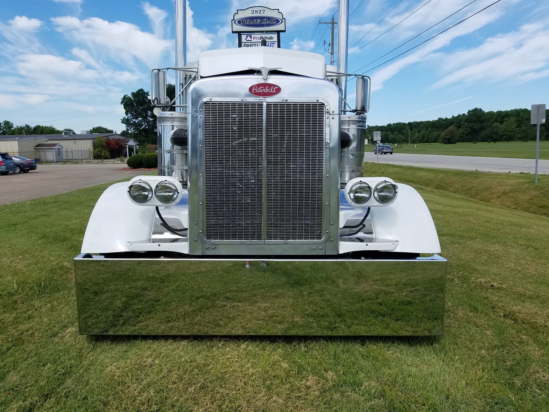White Peterbilt semi-truck with chrome grill and bumper, parked on grass, blue sky background.