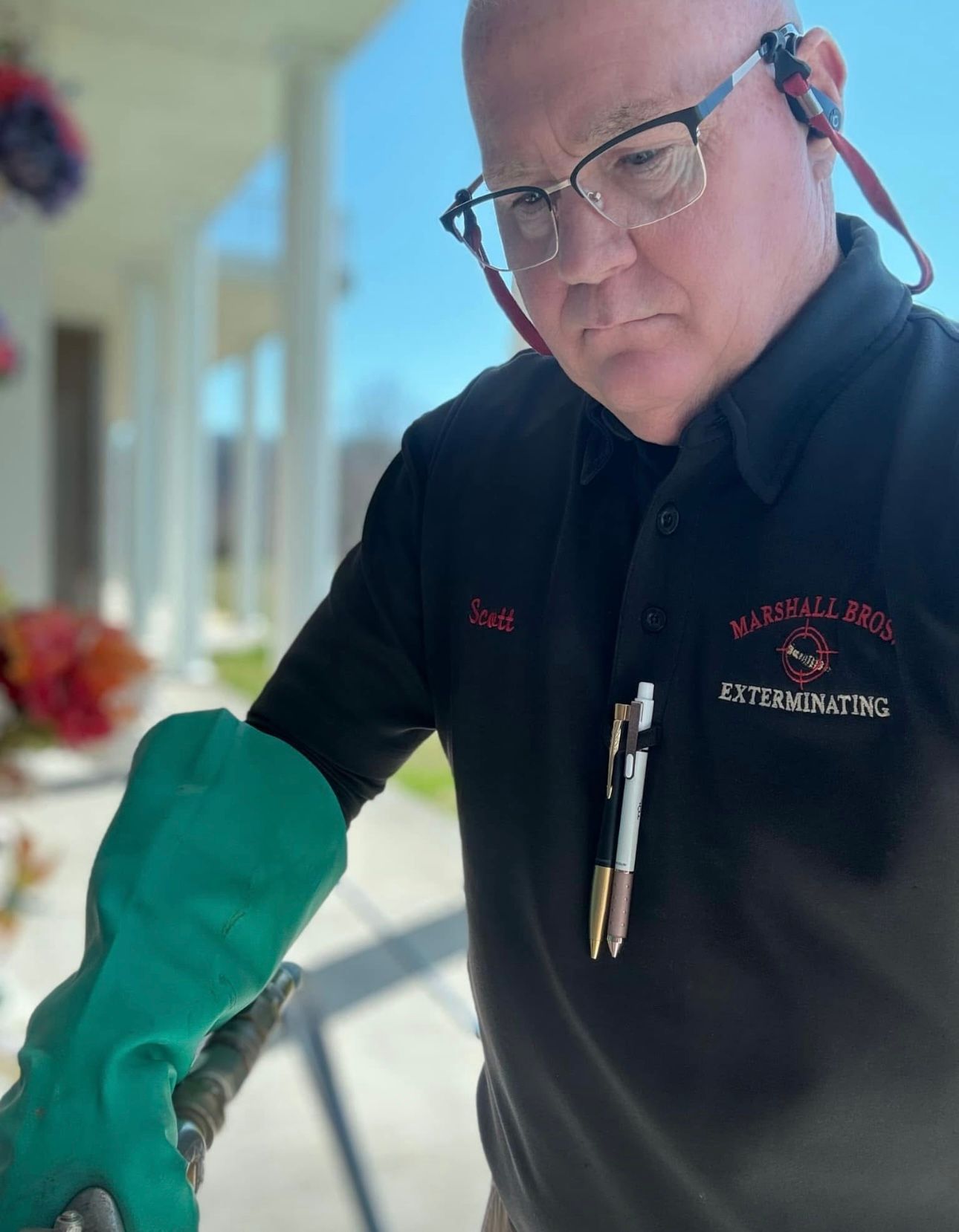 Man in black shirt with gloves, using equipment outside a building.