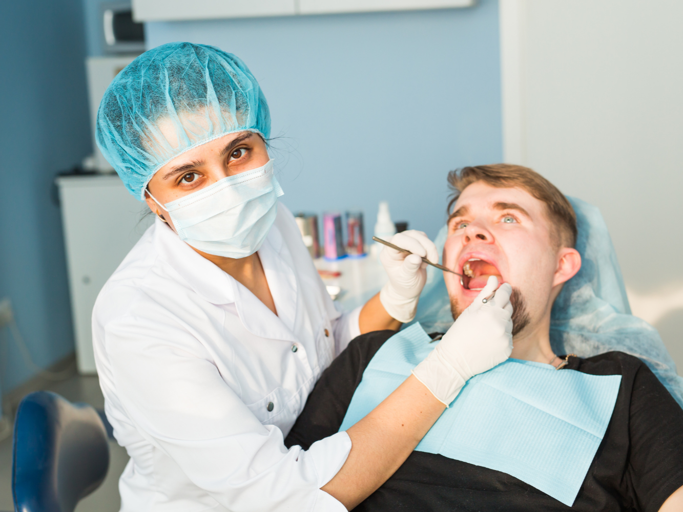 Dentist examining a patient's mouth with tools in a dental office.