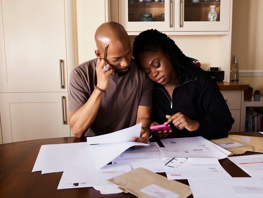 Two people reviewing papers at a table, leaning together over a phone in a home kitchen.