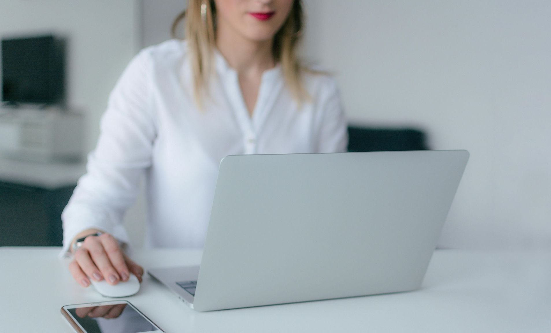 Woman in white shirt using laptop and mouse at a desk.