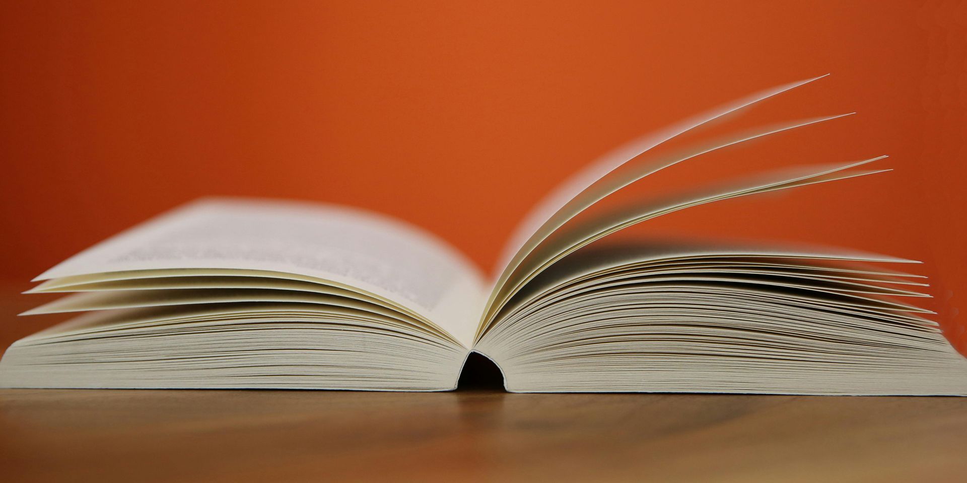 Open book with pages flipping against an orange backdrop.