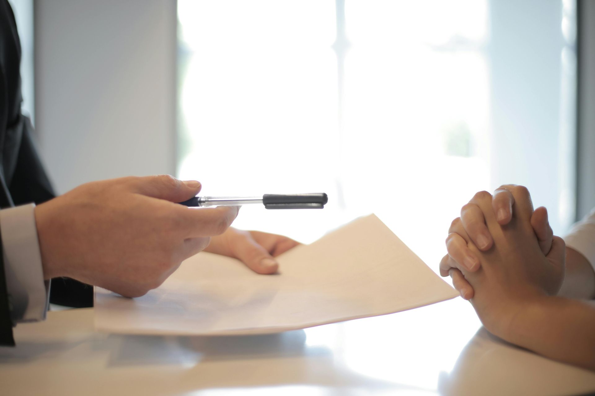 Person hands a document to another person; a pen is held over the document.