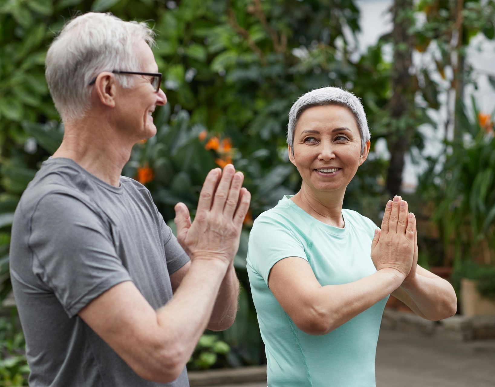 An older couple practicing yoga outdoors, hands together in prayer pose.