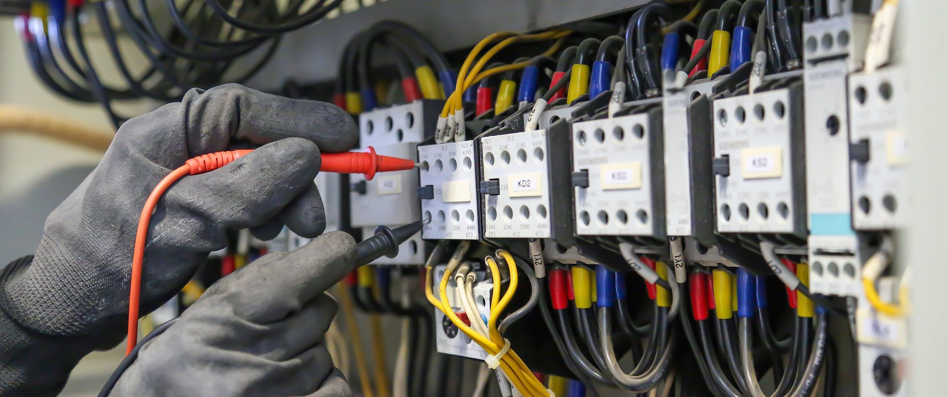 An electrician is working on an electrical box with a multimeter.