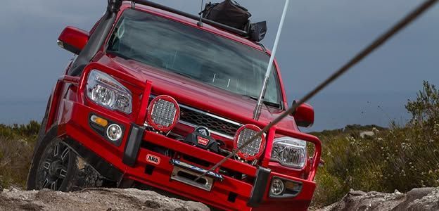 Red off-road truck climbing a rocky dirt trail, tilted on a steep incline