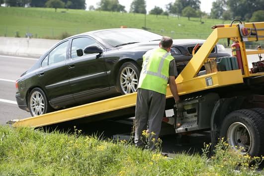 Tow truck hauling a broken-down black SUV on a roadside with two workers nearby