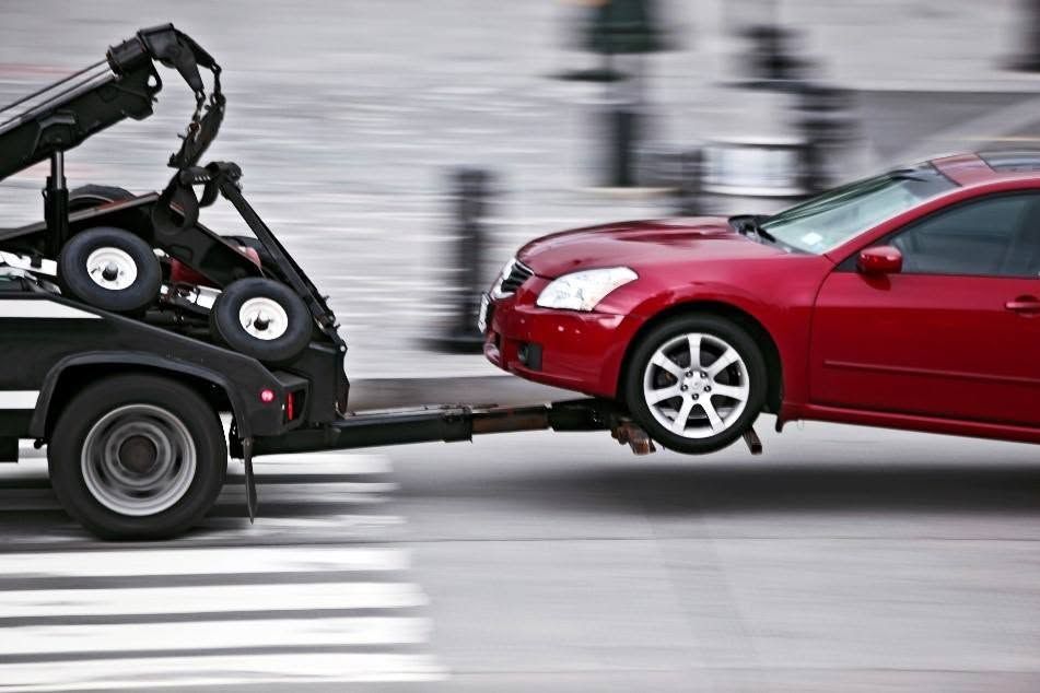 Tow truck towing a red car at a crosswalk, with motion blur in the background