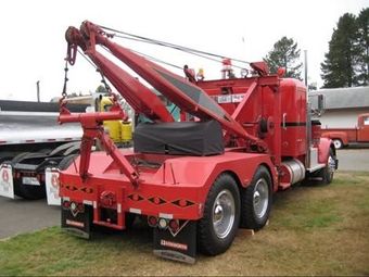 Red tow truck with raised boom parked on grass at a truck show