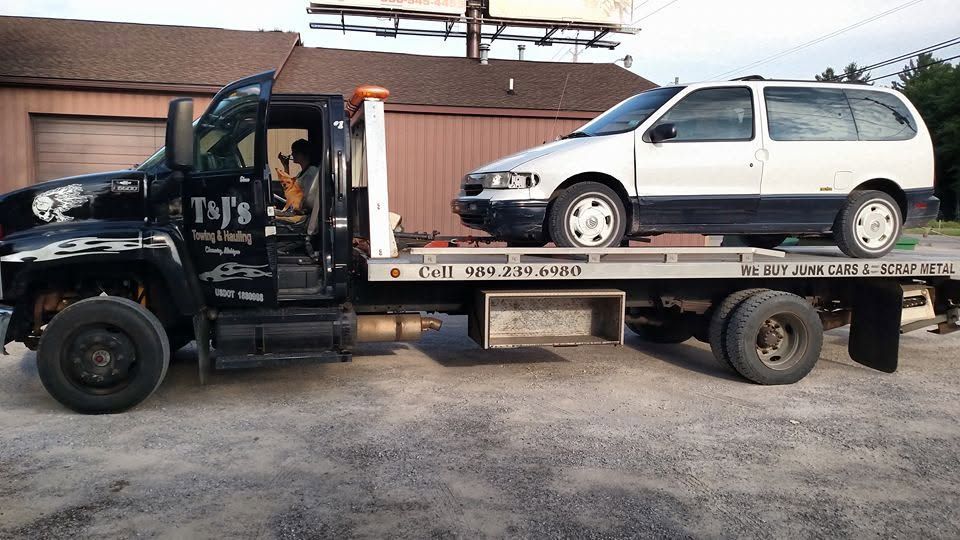 Tow truck carrying a silver minivan on a flatbed in a parking lot