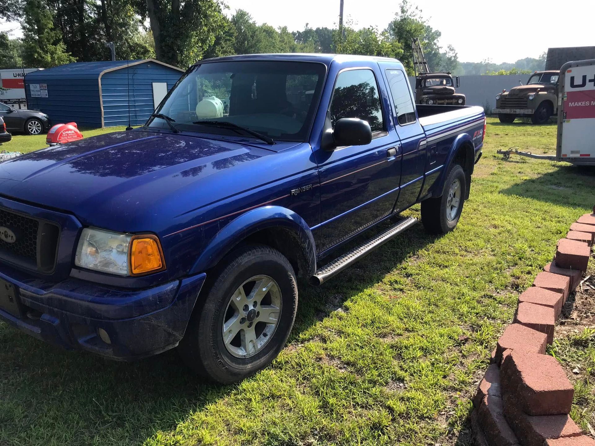 Blue pickup truck parked on grass beside a brick path in a sunny yard