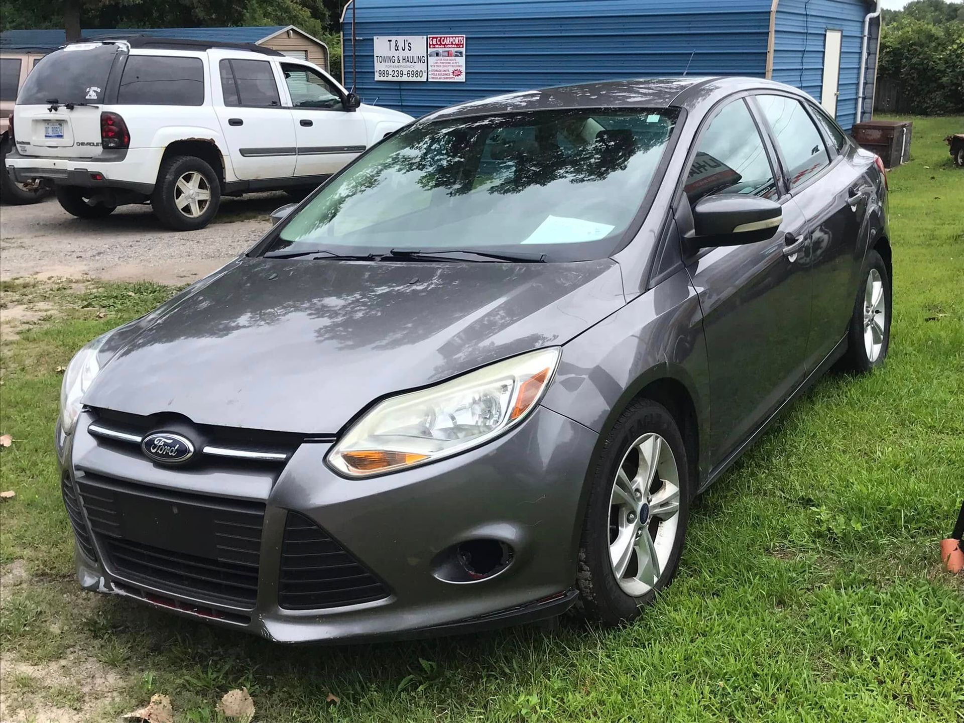 Gray Ford sedan parked on grass in front of a blue building, with a white SUV in the background