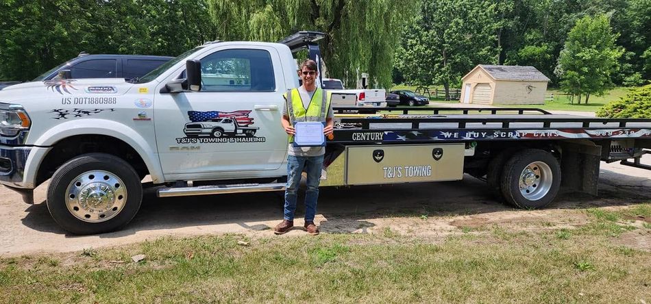 Tow truck parked on grass with a worker standing beside it in a roadside setting