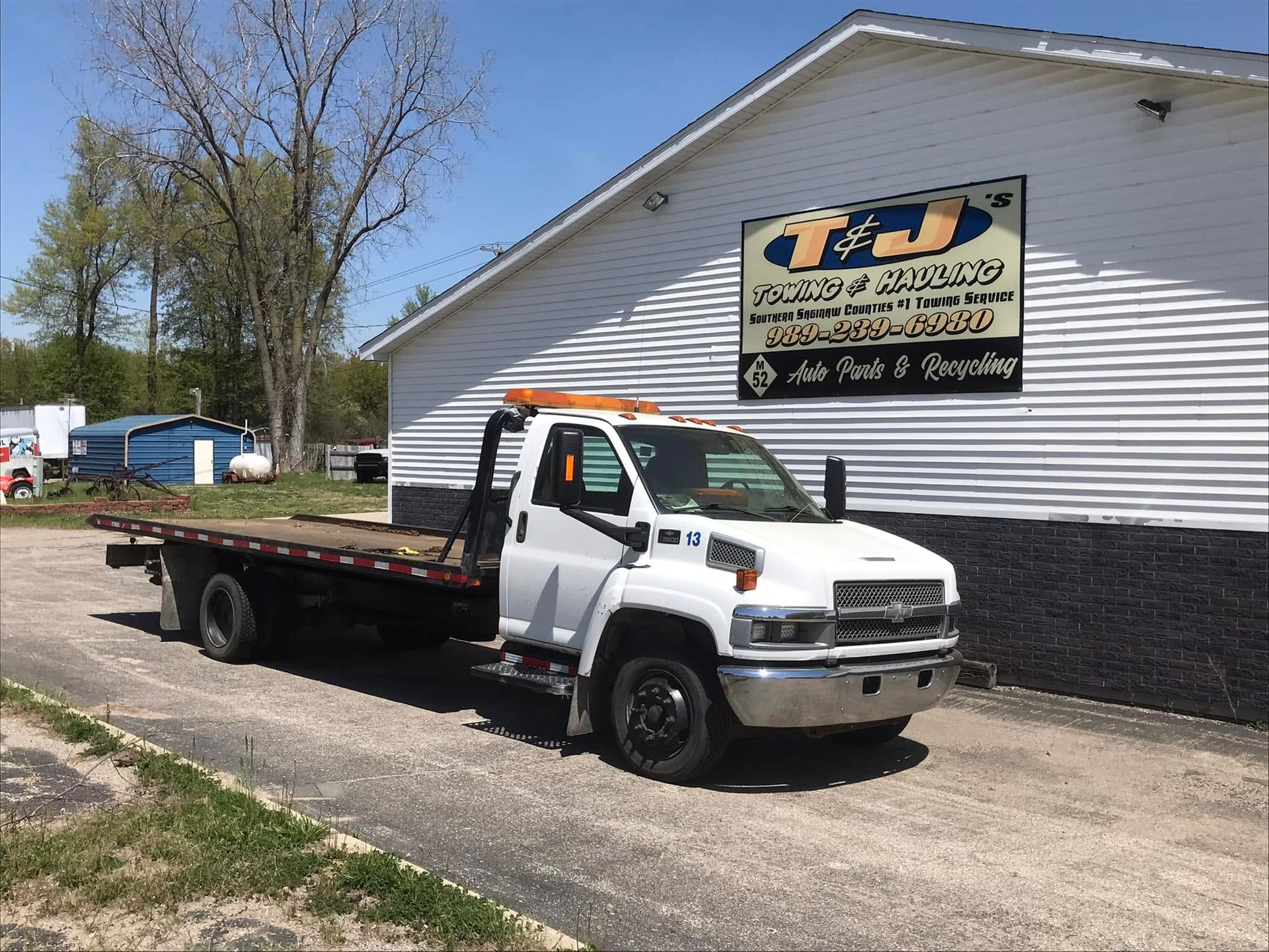 Tow truck parked beside a white building with a business sign on the wall