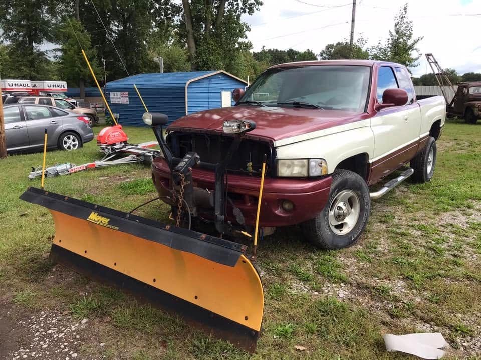Red pickup truck with front snow plow parked on a grassy lot