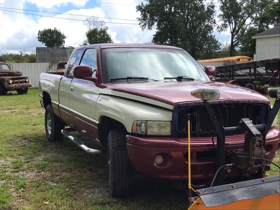Maroon and silver pickup truck with snowplow parked on grass near a barnyard.