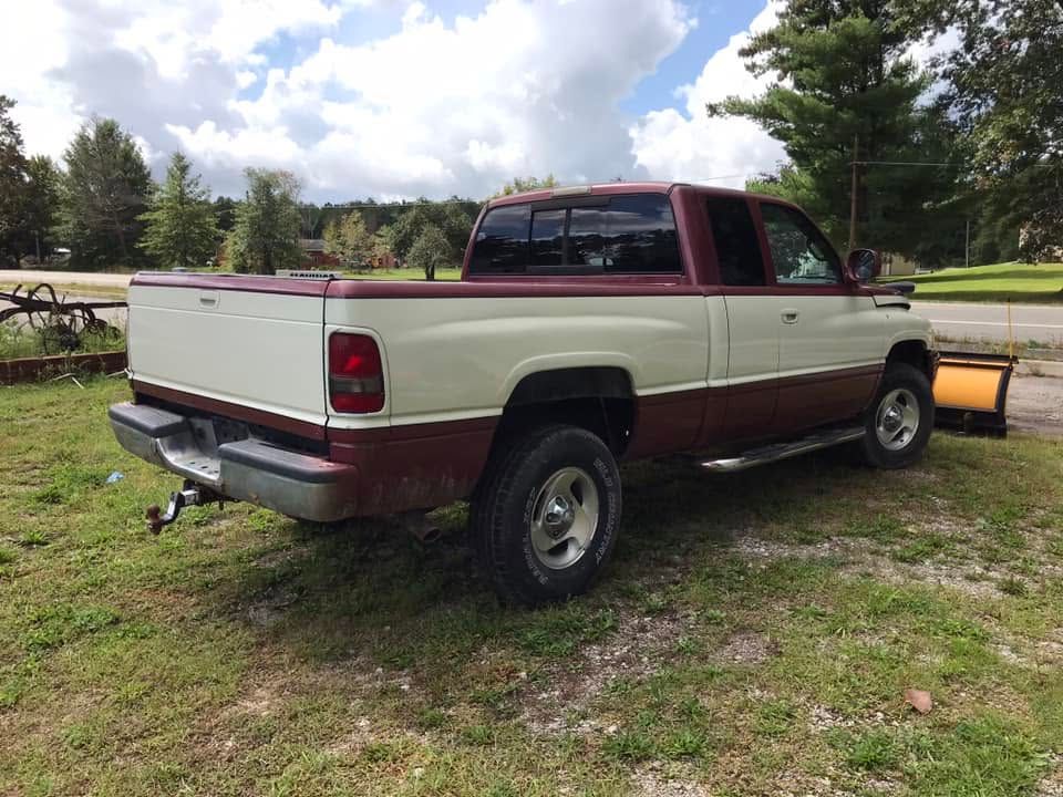 Maroon and white pickup truck parked on grass near a road with trees and cloudy sky.