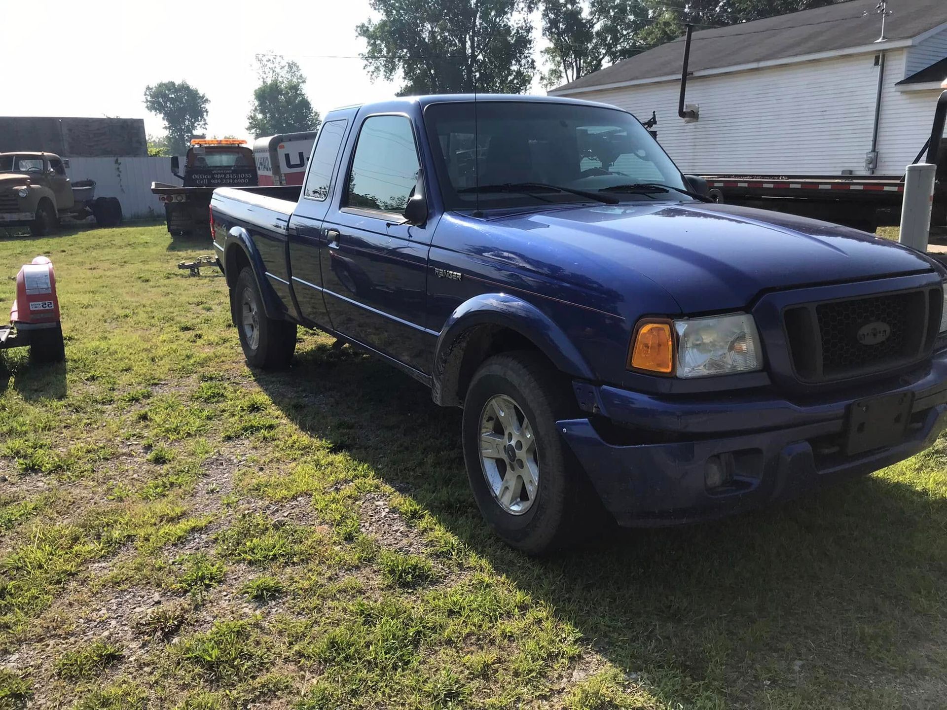 Blue Ford pickup truck parked on grass beside a building on a sunny day