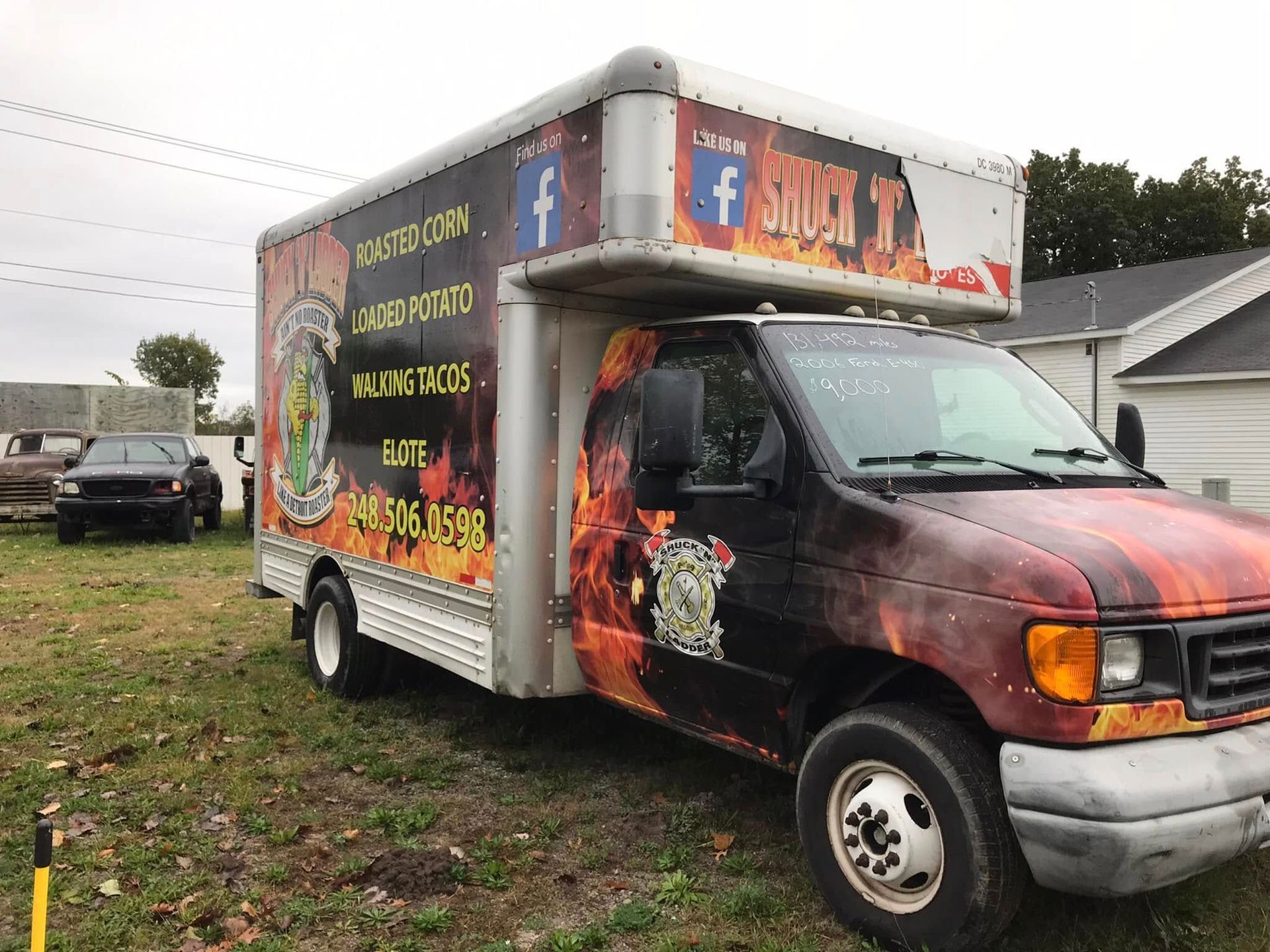 Food truck with flame graphics parked on a grassy lot, with a person visible in the driver’s seat.